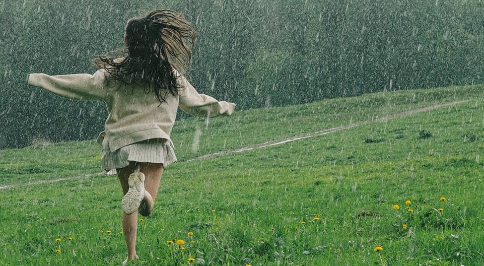 a person running in a grass field while raining